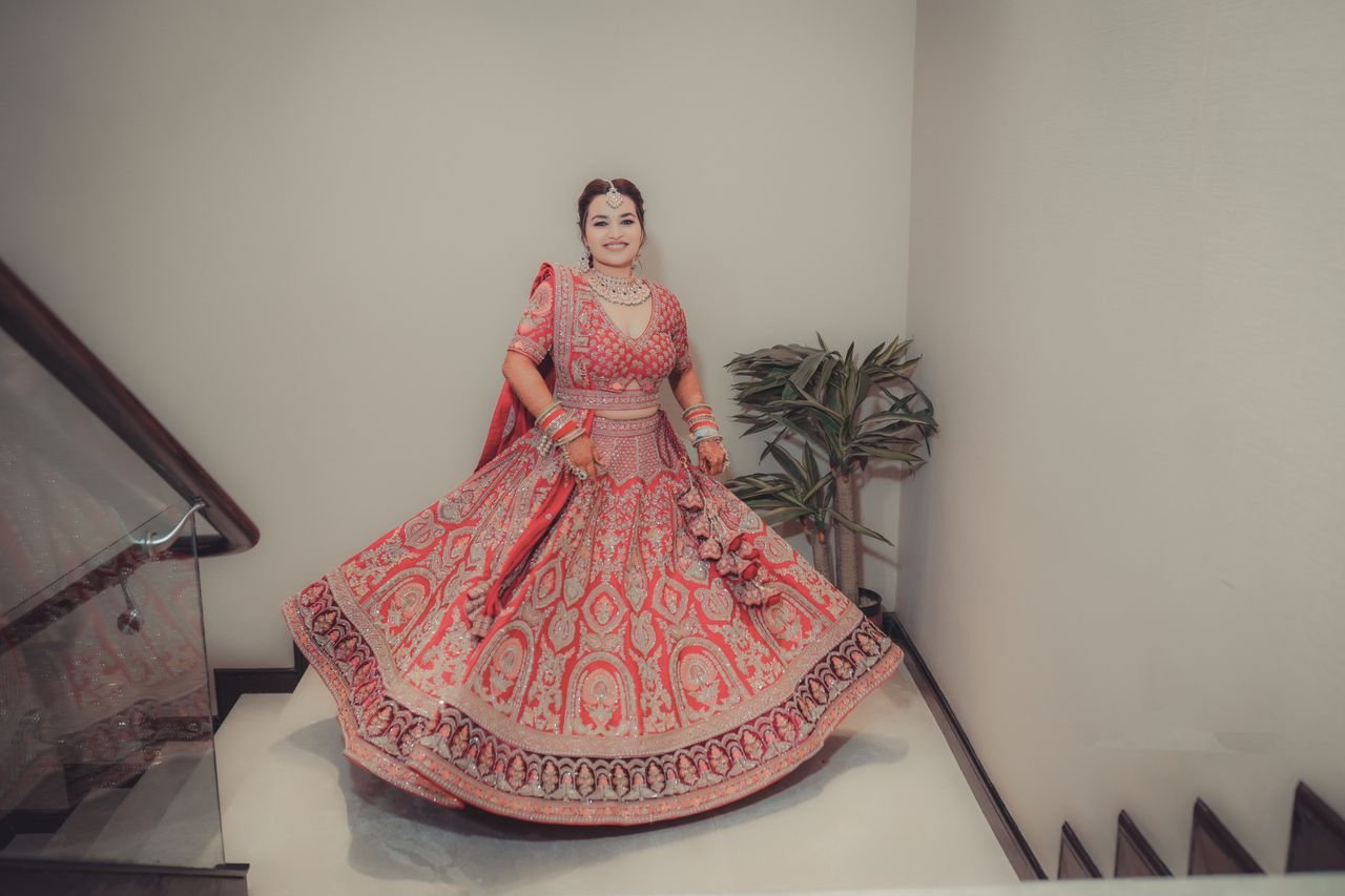 Smiling bride in ornate red lehenga posing indoors on her wedding day.