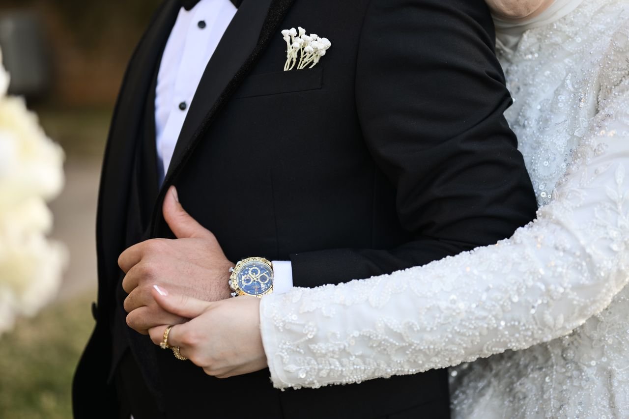 Close-up view of a wedding couple embracing, showcasing elegant attire and a luxury watch.