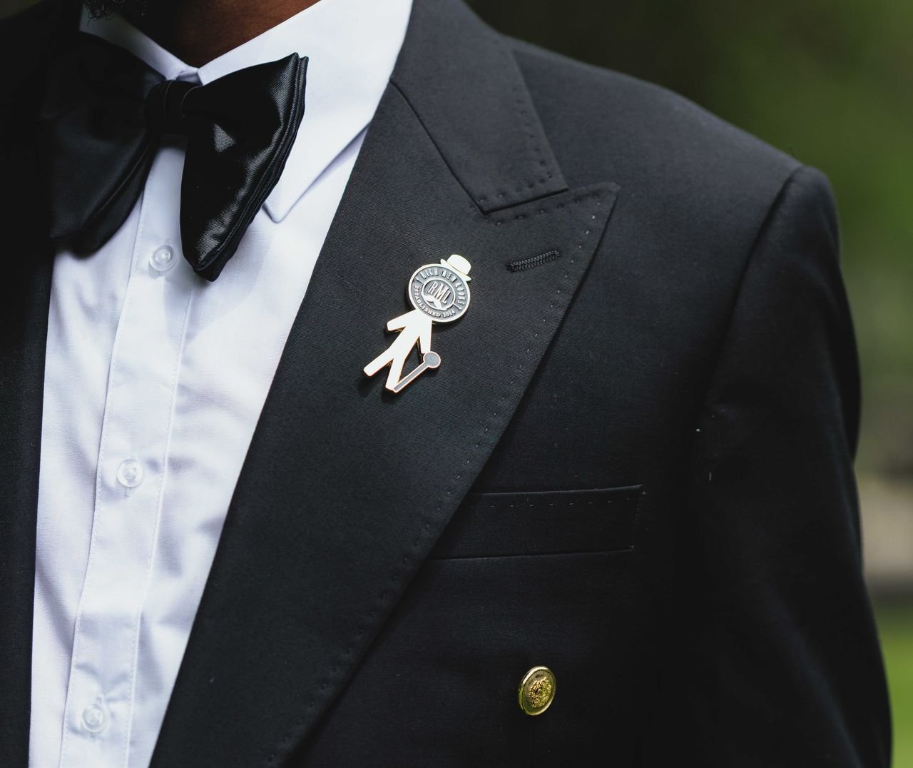 Close-up of a tuxedo featuring a unique lapel pin and black bow tie, exuding elegance and style.