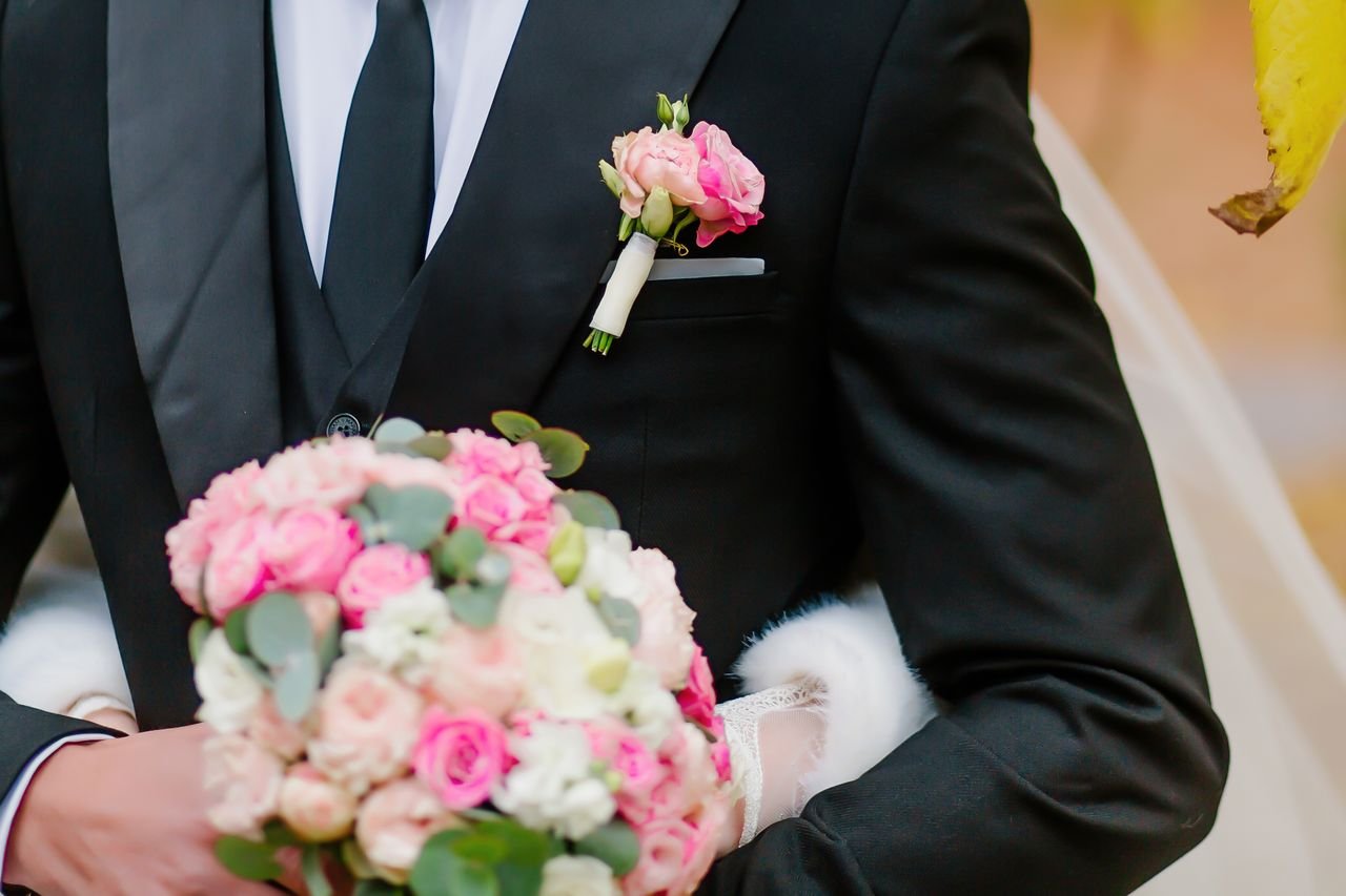 Close-up of a groom holding a vibrant pink rose bouquet at a wedding.