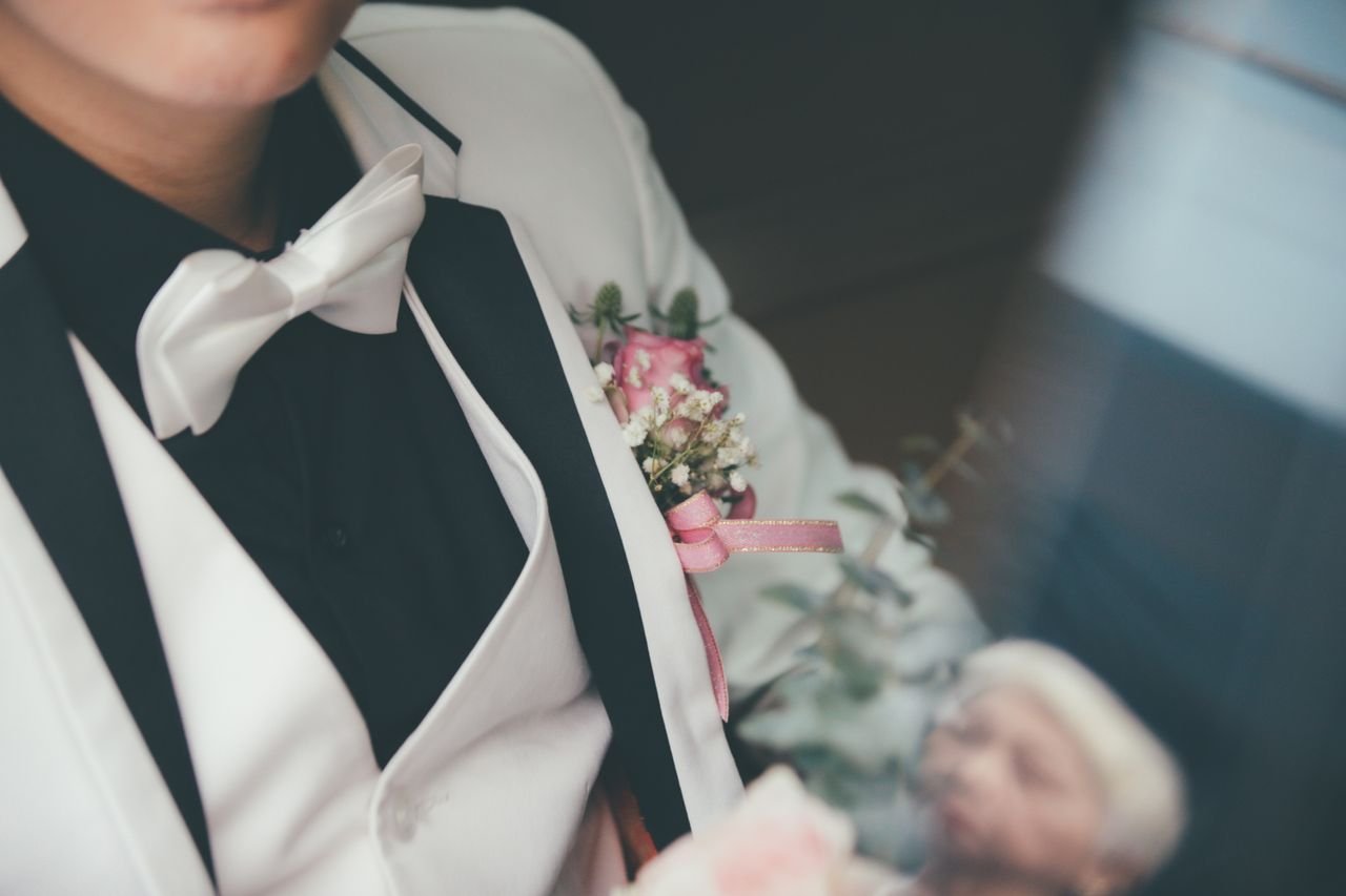 A groom in a tuxedo with a boutonniere reflecting an elderly woman. Perfect wedding moment.