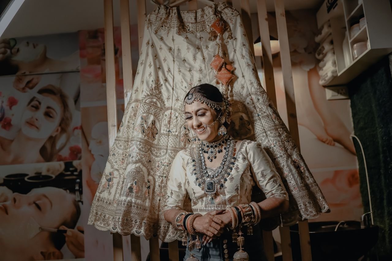 An Indian bride standing elegantly with traditional jewelry and wedding dress indoors.